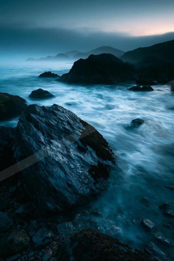 A black-toned moody photograph of promontory, seashore, cliff.