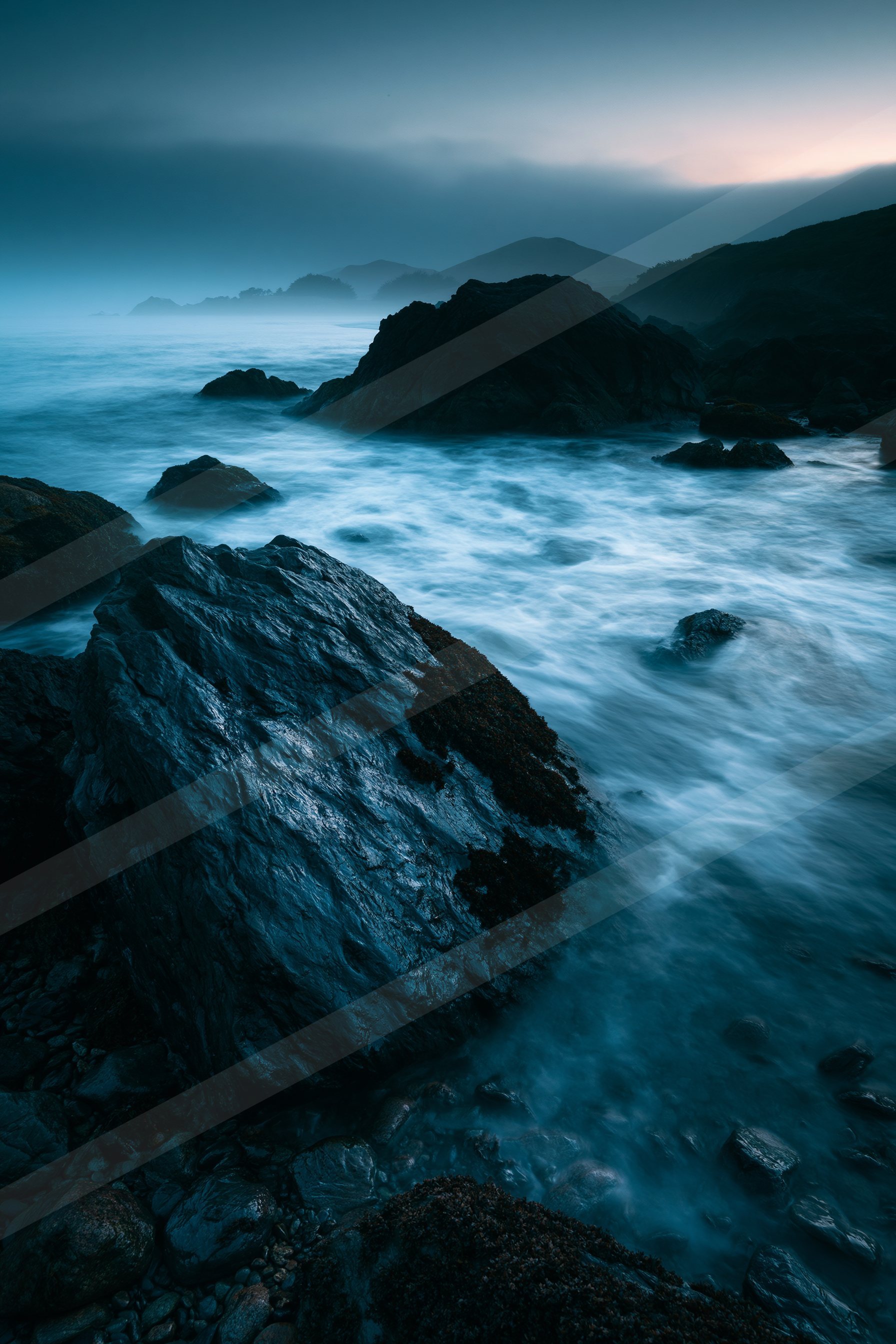 A blue hour long exposure water scene of a coastline, rocks.