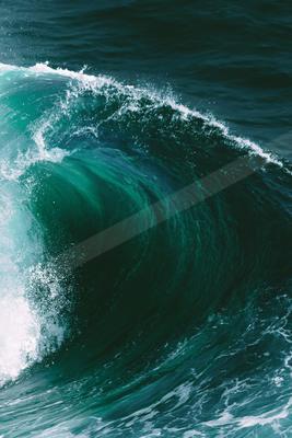 A powerful ocean wave curling with a crest of white foam, displaying vibrant shades of deep teal and turquoise in the sunlight.