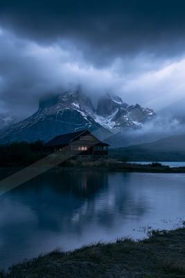 A blue hour water scene of lake, mountains, fog.