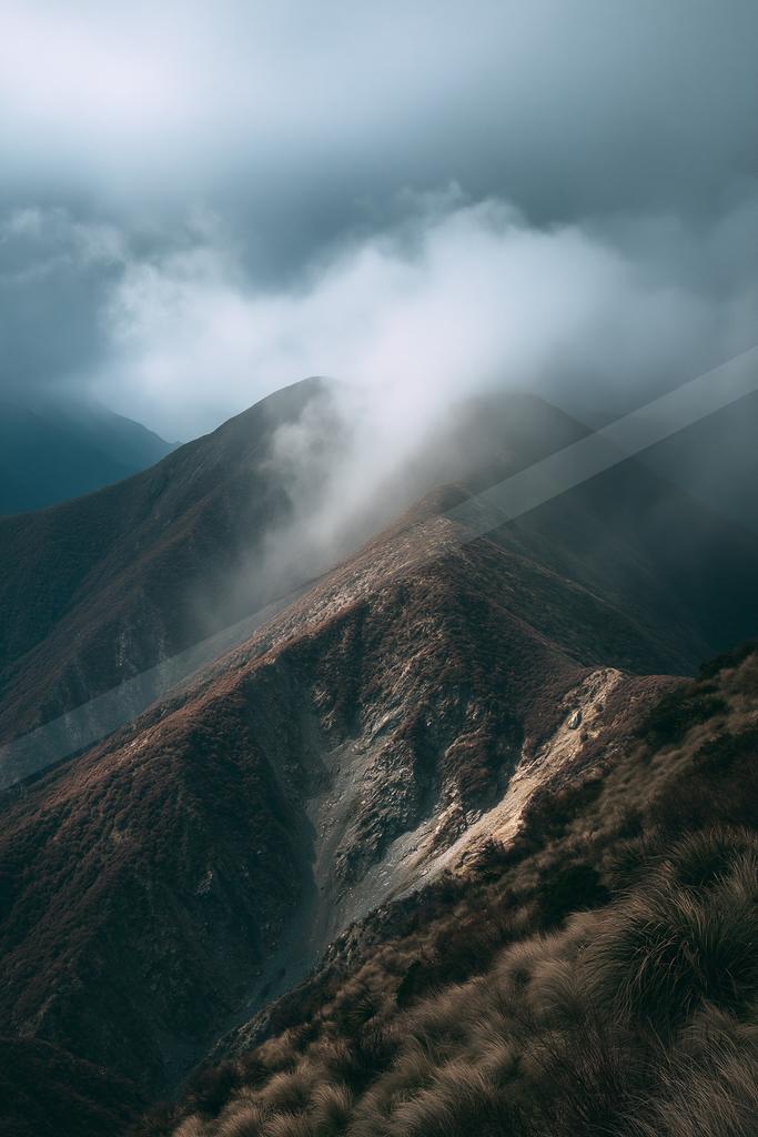 A dramatic landscape of mountains, fog.