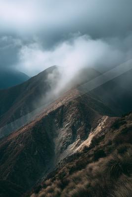 A rugged mountain range shrouded in mist and clouds, creating a mysterious atmosphere.