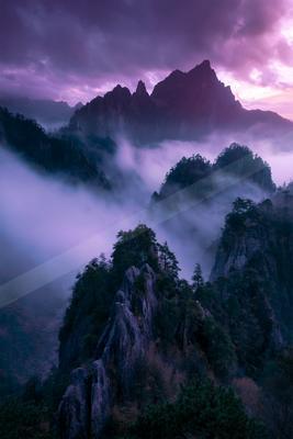 A dramatic landscape of mountains, fog.