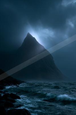 A sharp rocky mountain peak rises through dark storm clouds above a churning sea with white-capped waves and rocky shoreline in the foreground.