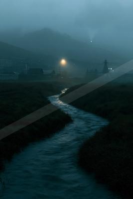 A winding river flows through a grassy landscape toward a foggy industrial town at dusk, with a single streetlight glowing in the mist and hills in the distance
