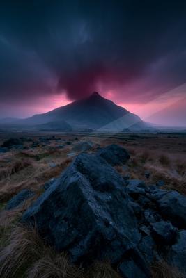 A dramatic landscape of mountains, storm, sunrise.