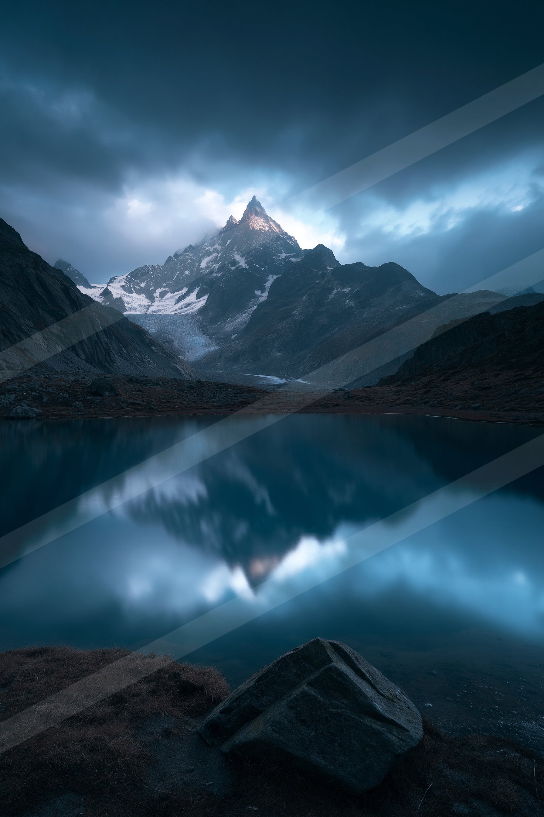 A majestic snow-capped mountain peak is mirrored perfectly in a tranquil lake, surrounded by rugged terrain under a moody twilight sky.