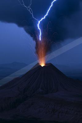 A volcano erupts at night, illuminated by a striking lightning bolt and glowing lava.