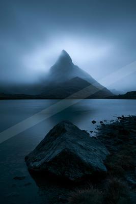 A blue hour long exposure landscape of mountains, lake, fog.