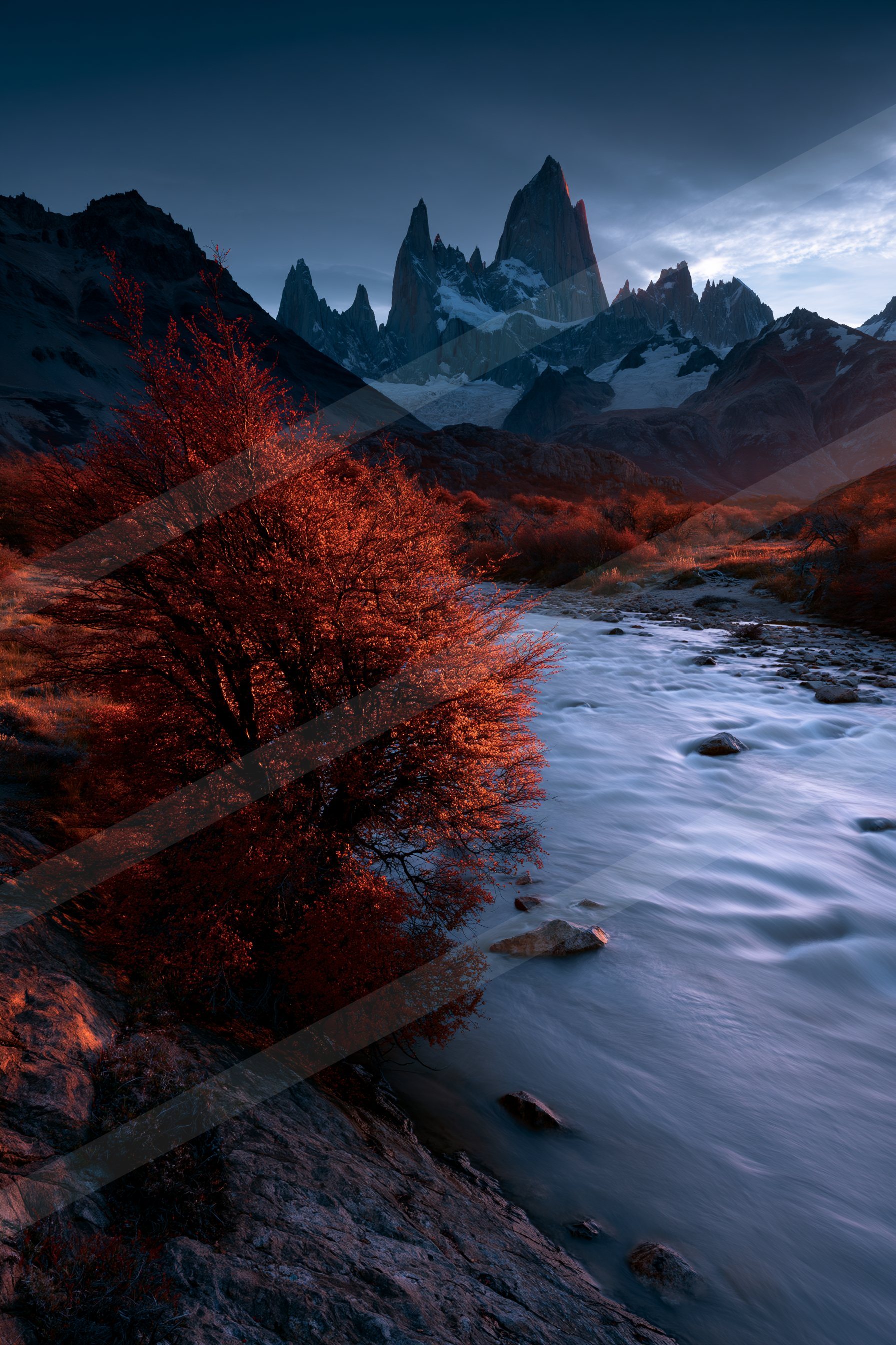 A serene river flows past vibrant red autumn trees, set against the backdrop of majestic snow-capped mountains under a twilight sky.