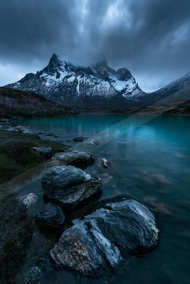 A blue hour long exposure water scene of lake, mountains, rocks.