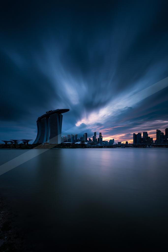 A black-toned moody photograph of pier, breakwater, fountain.