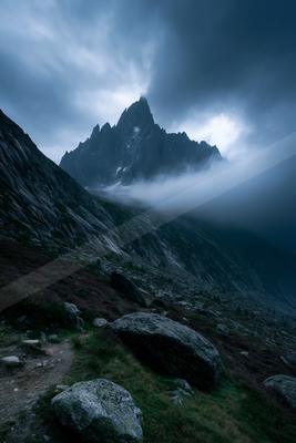 A dramatic landscape of mountains, fog.