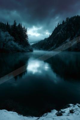 A serene winter landscape featuring a calm lake reflecting a dramatic, cloudy sky, surrounded by snow-dusted evergreen forests and rocky mountains.