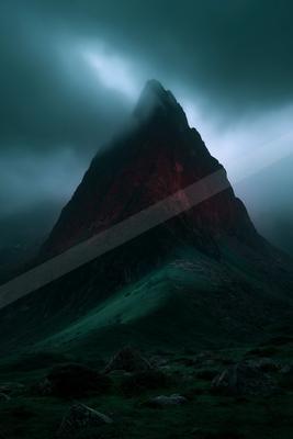 A sharp rocky mountain peak rises through thick swirling fog, its lower slopes covered in green vegetation and foreground scattered with boulders under a moody 