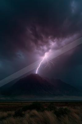 A powerful lightning bolt strikes the summit of a dark mountain under a turbulent purple and black stormy sky, with dry grass in the foreground.