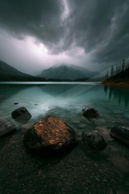 A serene water scene of lake, storm, mountains.