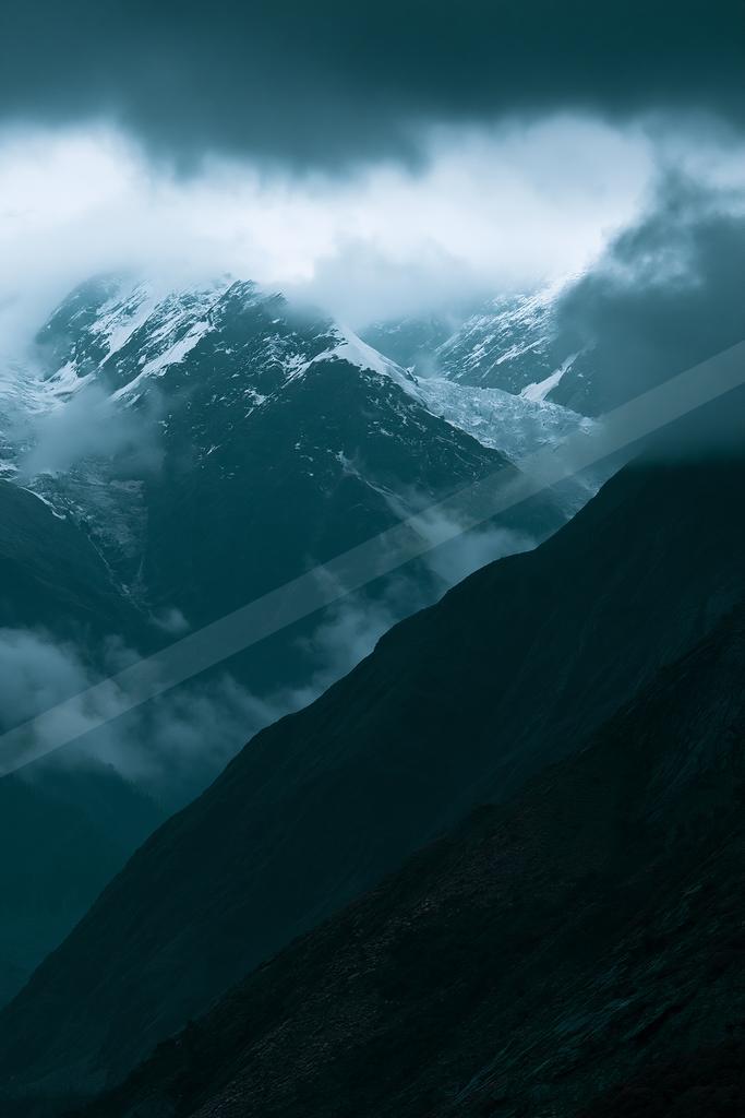 A dramatic landscape of mountains, fog.