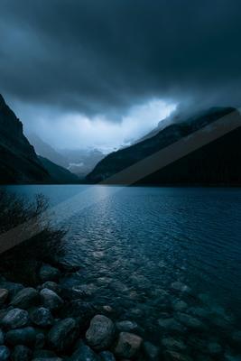 A blue hour long exposure water scene of lake, storm, mountains.