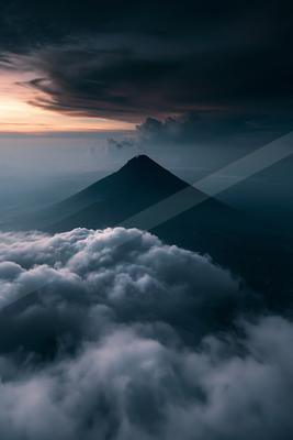 A dramatic landscape of mountains, clouds, sunrise.