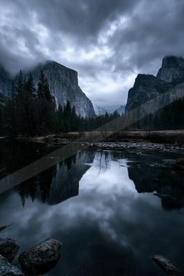 A serene lake mirrors towering mountain peaks under a moody sky, creating a symmetrical natural masterpiece.