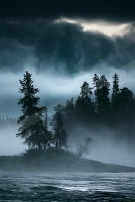 A dramatic sky scene of storm, trees, lake.