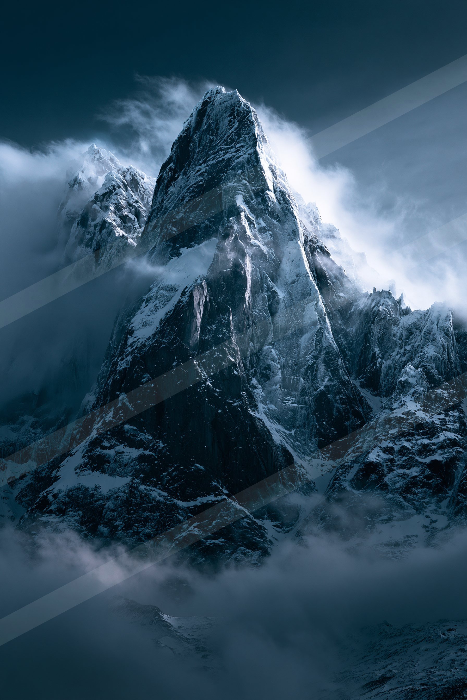 A towering snow-covered mountain peak piercing through a dense layer of clouds at dusk.