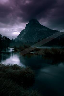 A powerful mountain peak rises under brooding purple storm clouds, with a smooth flowing river in the foreground and a dense forest at its base.
