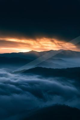 A blue hour sky scene of sunrise, mountains, clouds.