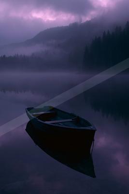 A wooden rowboat floats on the calm, reflective surface of a misty lake surrounded by a foggy forested mountain under a purple-hued cloudy sky.