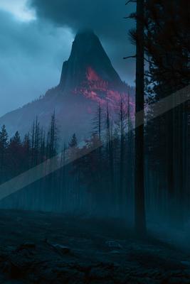 A towering mountain peak bathed in pink light rises above a dense, misty forest at night. The scene is atmospheric with dark silhouettes of trees and foggy surr