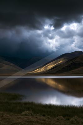 A moody water scene of lake, storm, mountains.