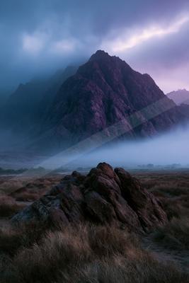 A dramatic landscape of mountains, fog.