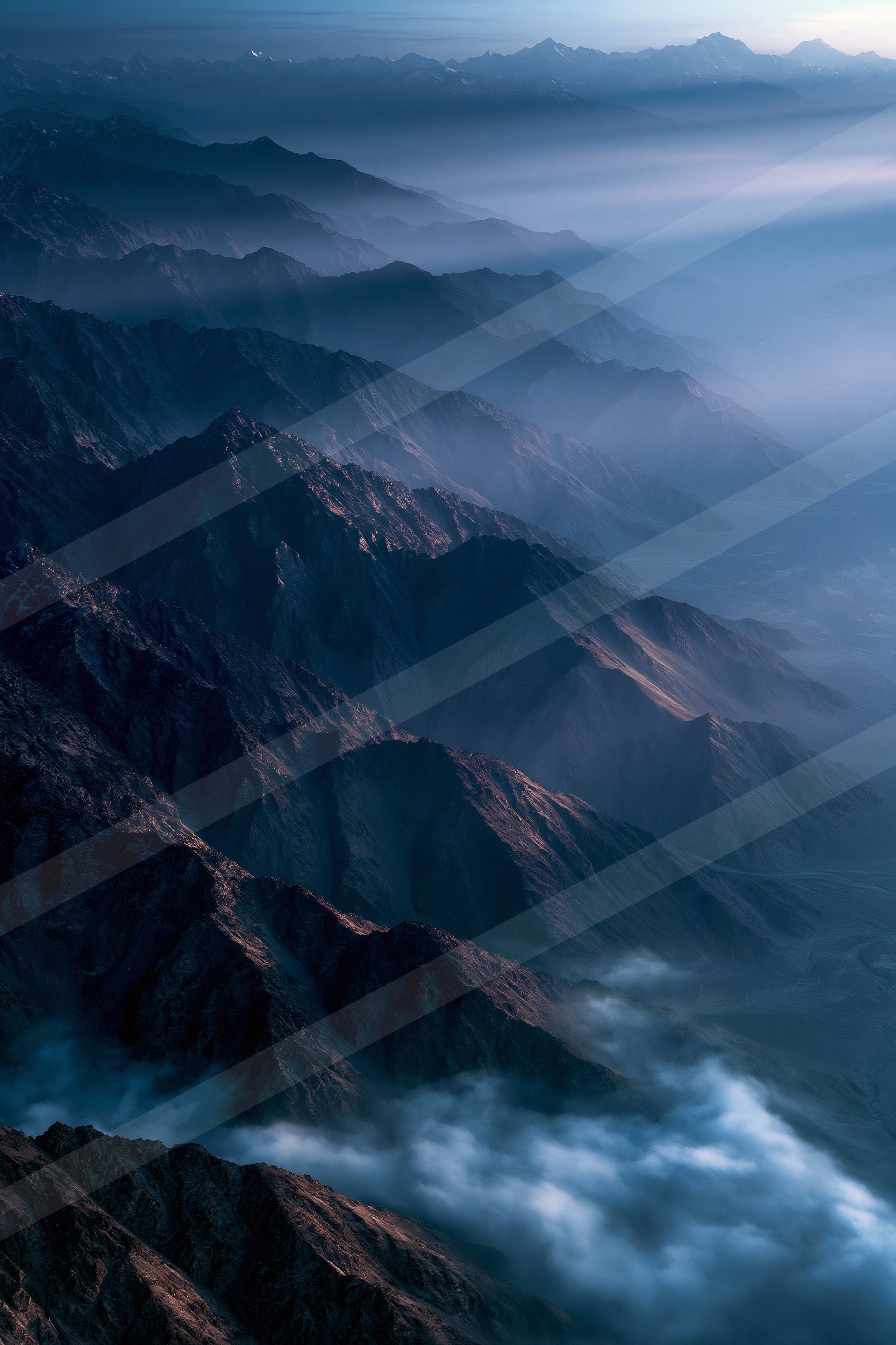 A stunning view of layered mountain ranges under a twilight blue sky, with mist filling the valleys and peaks silhouetted against the horizon.