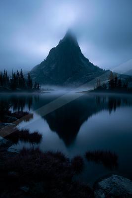 A blue hour long exposure water scene of lake, mountains, fog.
