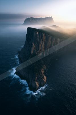A moody landscape of mountains, waterfall, ocean.