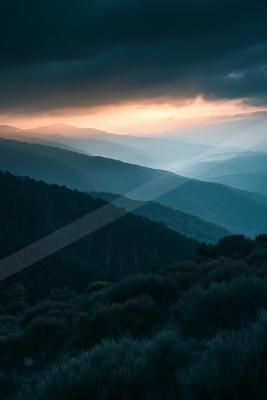 A blue hour minimalist landscape of mountains, valley, clouds.