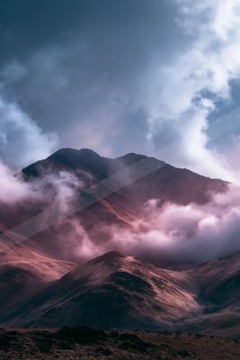 A dramatic landscape of mountains, fog.