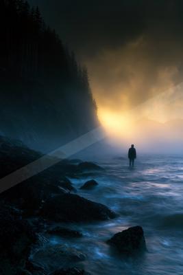 A lone silhouette stands in shallow water near a rocky shore under a glowing sunset, surrounded by mist and forested cliffs.