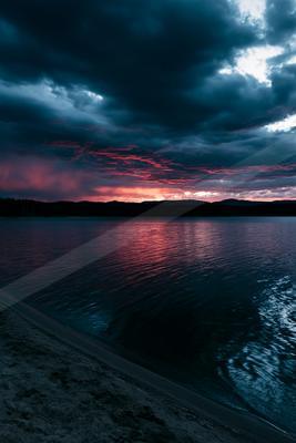 A blue hour water scene of lake, clouds, sunrise.