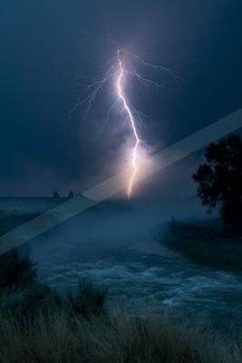 A powerful lightning bolt strikes the ground in the distance over a misty river during a stormy night, illuminating the dark landscape with a bright flash.