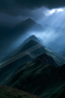 Moody atmospheric landscape of rugged mountain peaks shrouded in thick fog with dramatic crepuscular rays piercing through dark storm clouds from above.