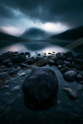 A blue hour long exposure water scene of lake, mountains, rocks.