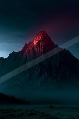 A jagged mountain peak dramatically illuminated with red light rises above a sea of fog under a dark night sky, with a dark forest visible in the foreground.
