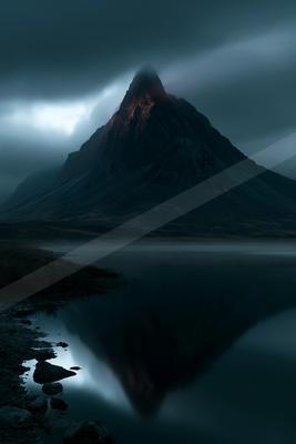 A sharp rocky mountain peak partially lit by a break in the dark stormy clouds rises above a perfectly still lake that mirrors its silhouette, with rocky shorel