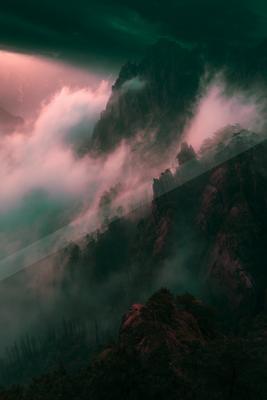 A dramatic landscape of mountains, clouds, fog.