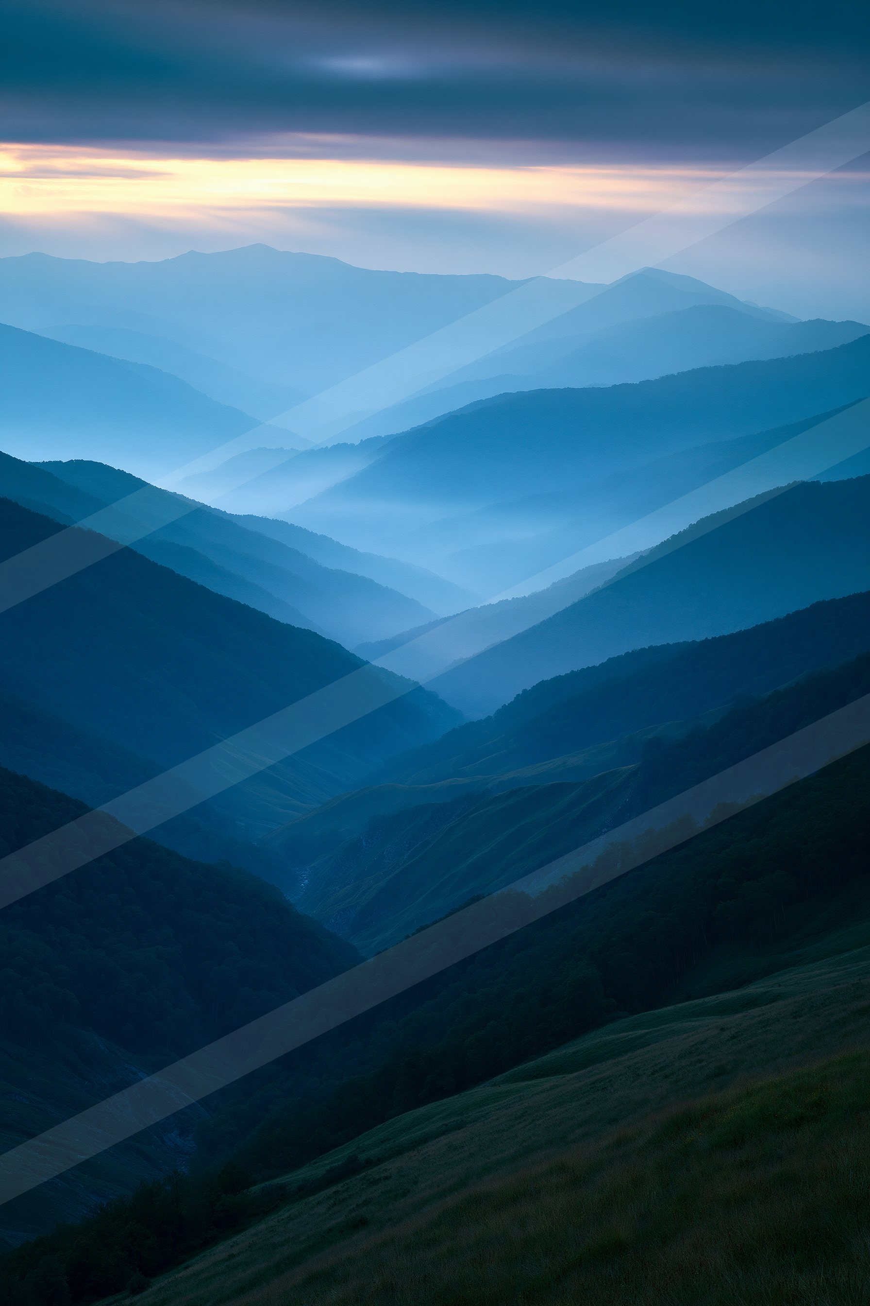 A serene mountain landscape bathed in the soft glow of dusk, featuring layered peaks shrouded in mist and a colorful sky transitioning from blue to yellow.