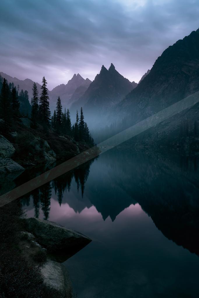 A blue hour water scene of lake, mountains, fog.