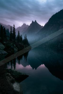 A blue hour water scene of lake, mountains, fog.
