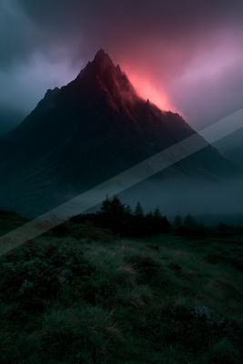 A sharp rocky mountain peak rises through thick fog and low clouds, illuminated by an intense red and pink glow from behind, with a dark foreground of moorland 